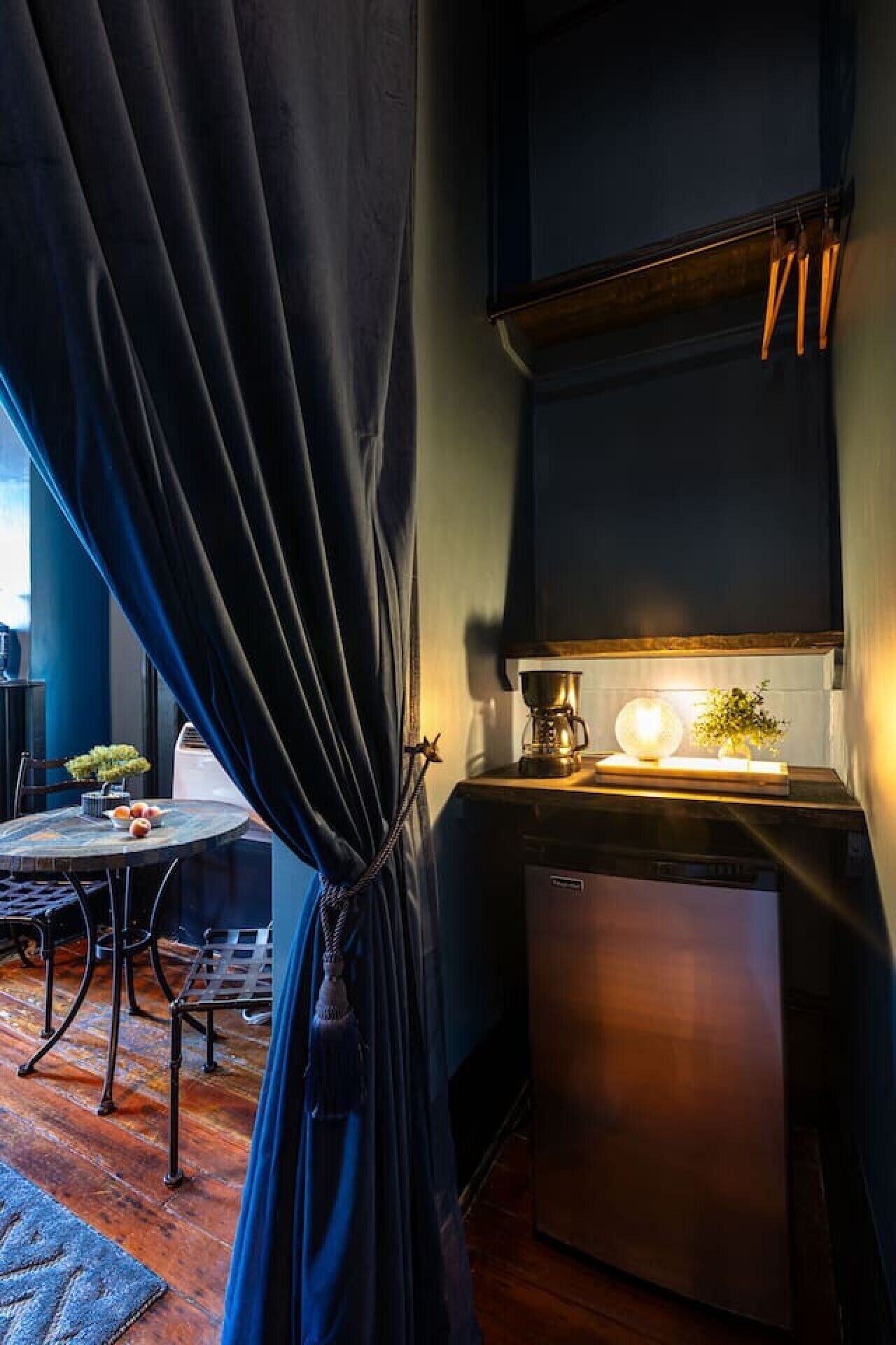 Une cuisine compacte équipée d’une machine à café, d’un petit réfrigérateur et d’un coin repas avec une table et des chaises.