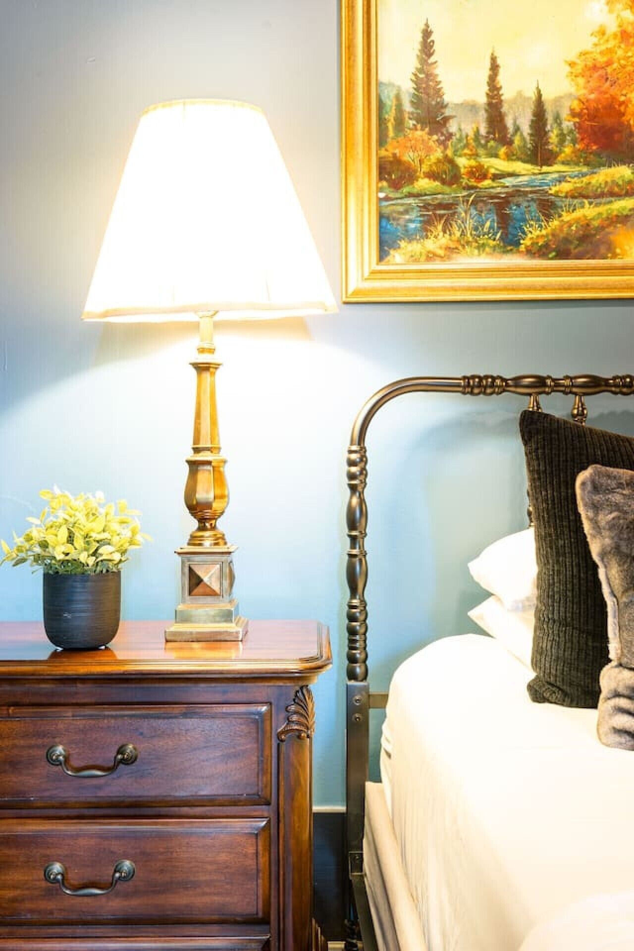 A bedroom with a bed, a nightstand with a lamp, a dresser, and a painting on the wall.