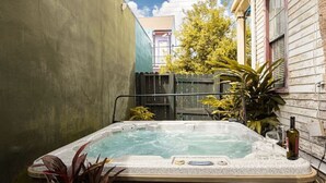 Een hottub in een achtertuin met een houten terras, een potplant en een fles wijn.