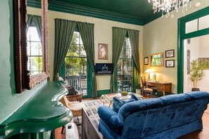A room with a green piano, a blue sofa, a chessboard, and a chandelier.