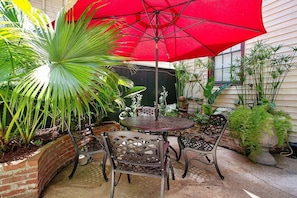 En terrasse med et rundt bord, stole, en rød parasol og forskellige planter.