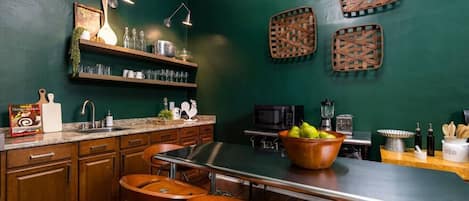 A kitchen with a central island, bar stools, a microwave, and a blender.