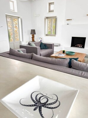 A modern living room with a sofa, coffee table, and a decorative glass table with a black octopus design. - Cycladic villa with panoramic sea & mountain view (Τοπική Κοινότητα Κώστου)