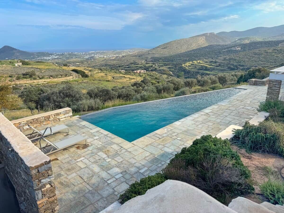 Una piscina con plataforma de piedra, rodeada por un muro de piedra y vegetación.