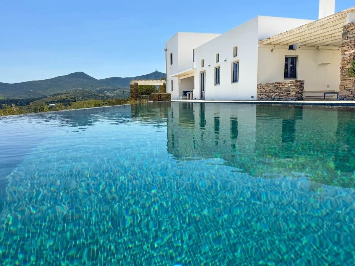 A modern building with a pool, clear water, and a mountainous backdrop.