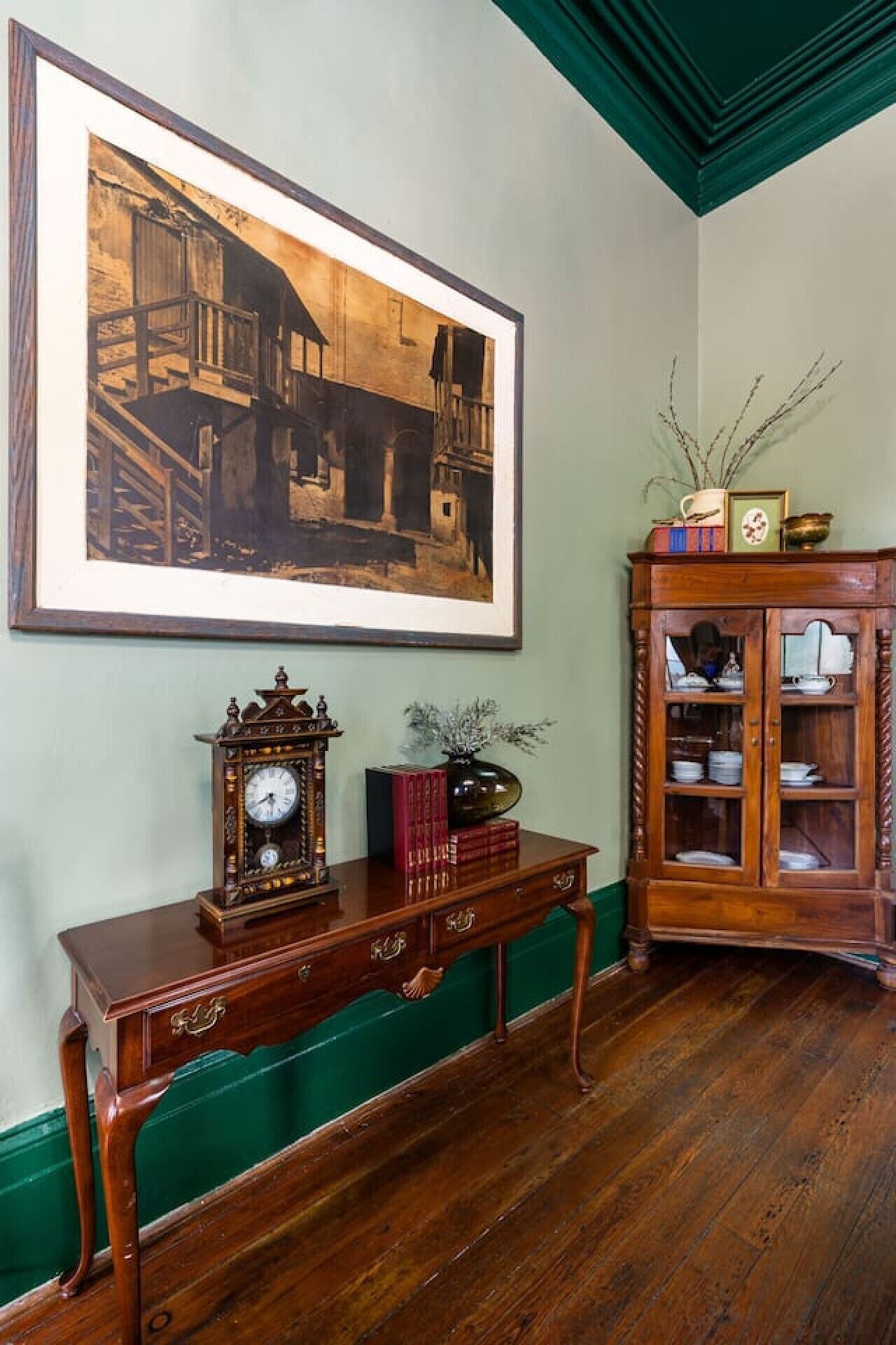 A room with a wooden console table, a framed picture on the wall, and a wooden cabinet with glass doors.