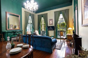 A room with a large bed, a dining table with plates and glasses, a chandelier, and a sign indicating the room's name.