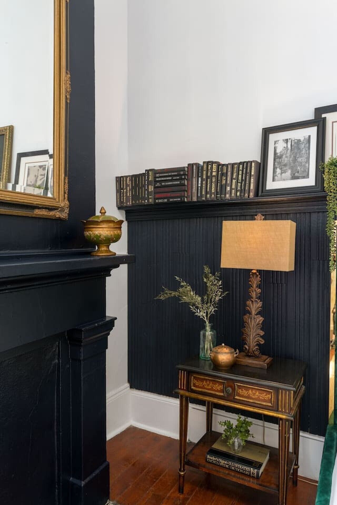 Ein Zimmer mit einem schwarzen Kamin, einem kleinen Holztisch mit Lampe und einem Bücherregal voller Bücher.