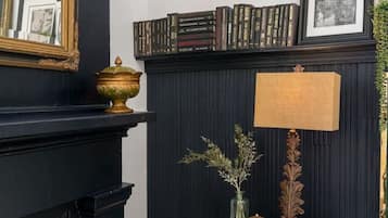 A room with a black fireplace, a small wooden table with a lamp, and a bookshelf filled with books.