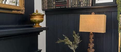 A room with a black fireplace, a small wooden table with a lamp, and a bookshelf filled with books.