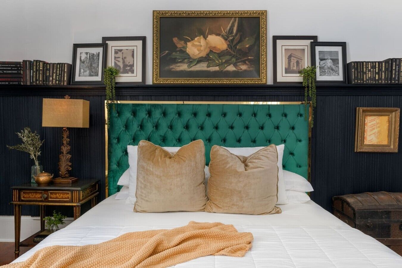 Een slaapkamer met een groen gewatteerd hoofdeinde, twee beige kussens, een witte spreidek en een beige plaid.