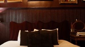 A hotel room with a bed, pillows, a wooden headboard, a nightstand with books, and a mirror. - Marigny Historic 1BD Steps to Jazz & Frenchmen (New Orleans)