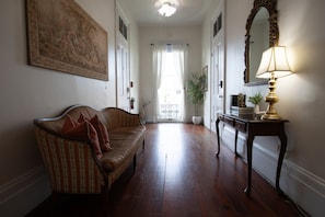A hallway with a sofa, a table with a lamp, and a large mirror.