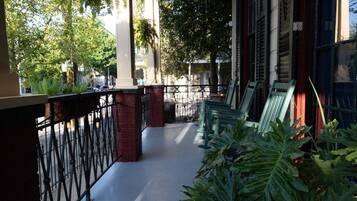 A covered outdoor area with a metal railing, green chairs, and potted plants.