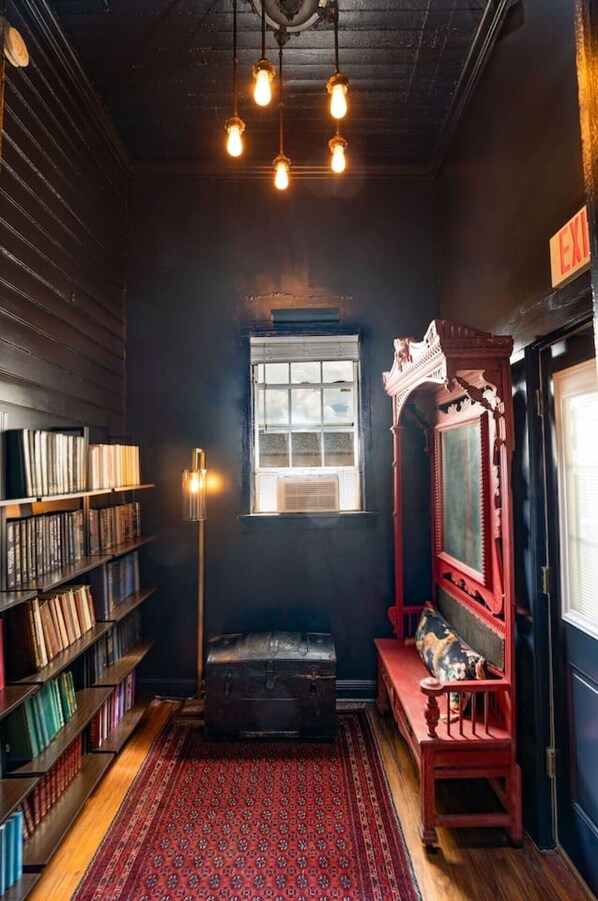 A room with a bookshelf, a red bench, a window, and a red wall.