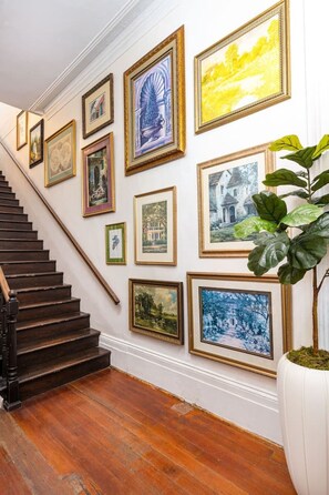 A staircase with a wooden handrail and a white wall adorned with framed artworks.
