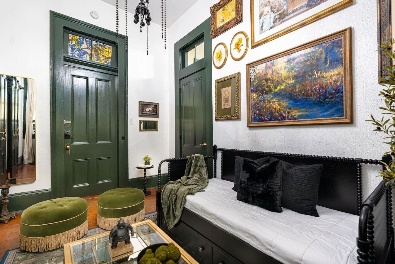 Een kamer met een bed, een groene poef, een tafeltje met een sculptuur en een schilderij aan de muur.