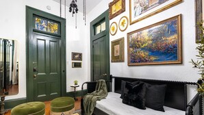 A room with a bed, a green ottoman, a small table with a sculpture, and a painting on the wall. - Historic Marigny 2BD | Walk to Music & Food (New Orleans)