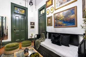 Una habitación con una cama, un reposapiés verde, una mesita con una escultura y un cuadro en la pared.