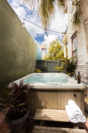 Un bain à remous dans un jardin, avec une terrasse en bois, une plante en pot et une bouteille de vin.