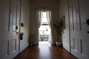 A hallway with wooden flooring, white doors, and a window with curtains.