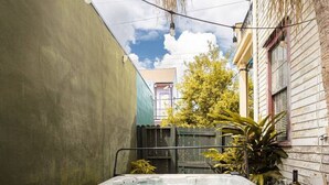 Un jacuzzi en un patio trasero con una terraza de madera, rodeado de plantas y un edificio.