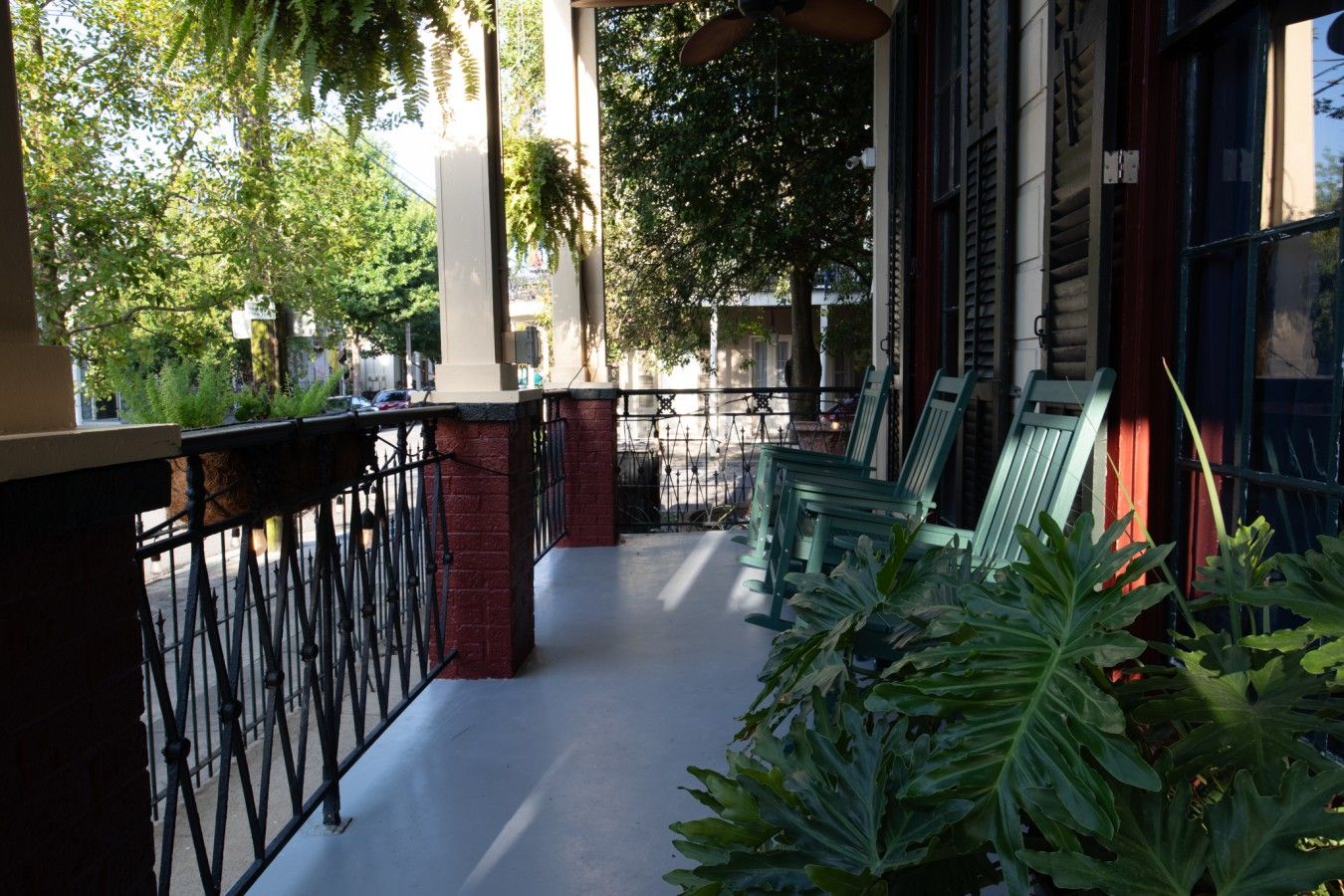 A covered outdoor area with a metal railing, green chairs, and potted plants.