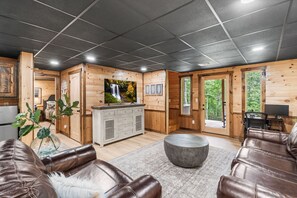 Een chaletinterieur met houten details, een open haard, leren zitplaatsen en een televisie.
