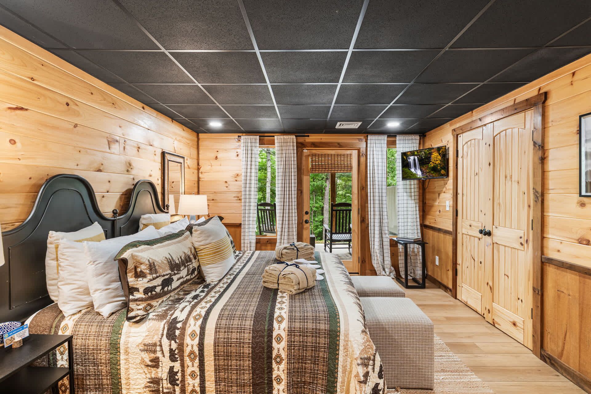 Un dormitorio de cabaña de madera con una cama, un televisor y vistas al exterior.