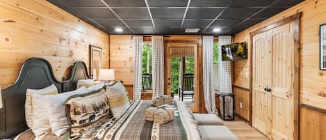 Un dormitorio de cabaña de madera con una cama, un televisor y vistas al exterior.
