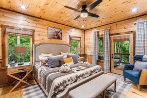 Ein Schlafzimmer in einer Holzhütte mit einem Bett, Nachttischen, einer Bank und einem Deckenventilator.