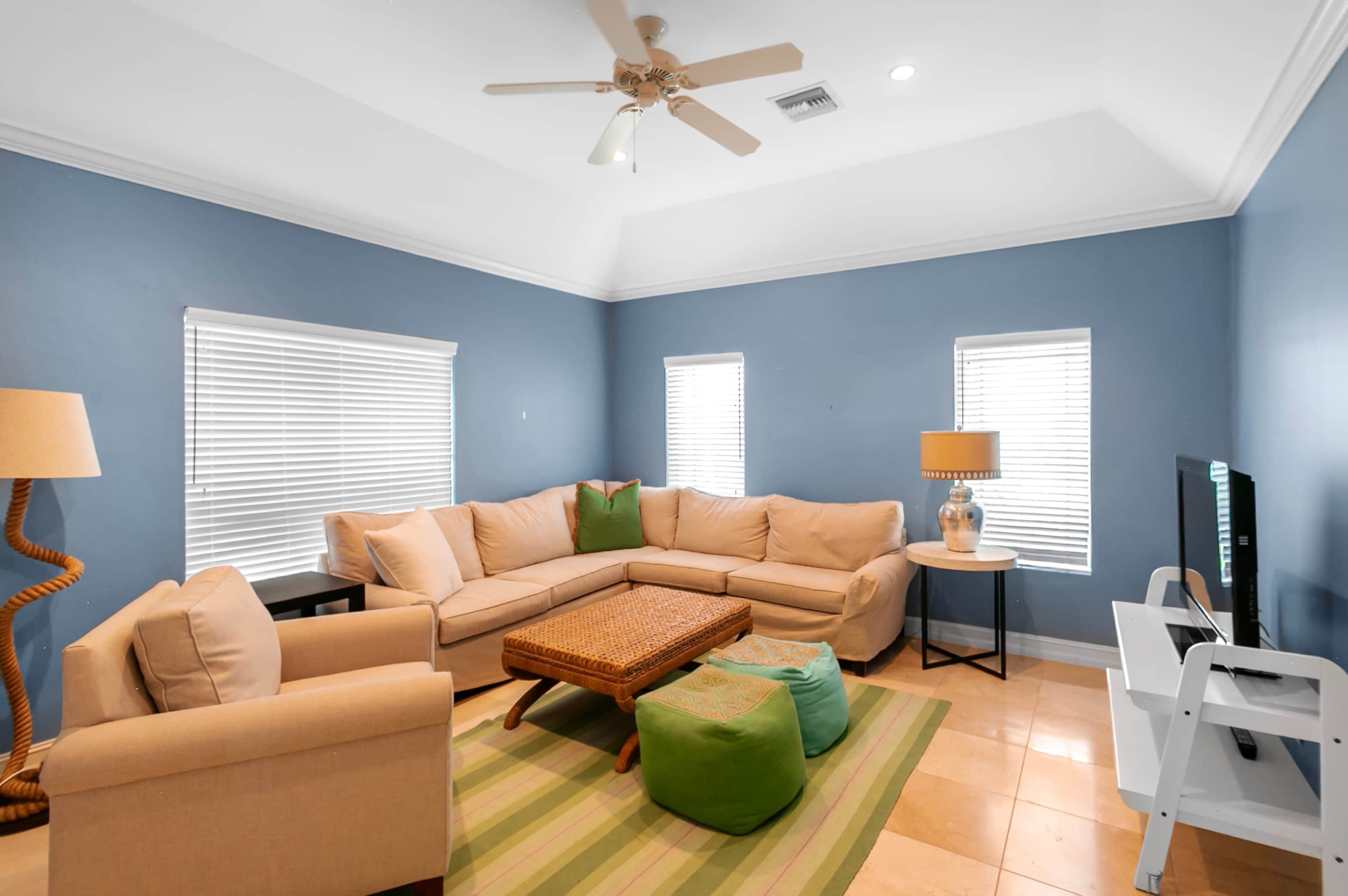 A living room with a sectional sofa, a coffee table, ottomans, a lamp, and a ceiling fan.