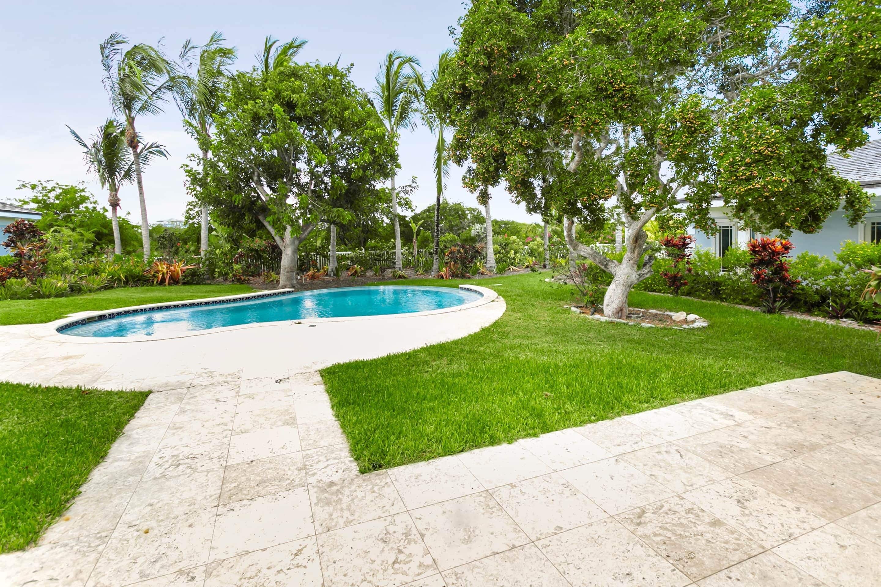 A swimming pool surrounded by a well-maintained lawn and various trees.