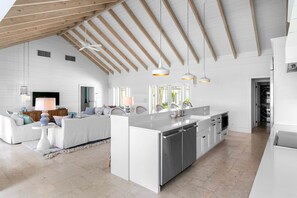 Una cocina amplia con una isla central, armarios blancos e iluminación colgante.