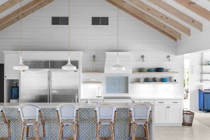 A modern kitchen with a central island, bar stools, pendant lighting, and a view of the outdoors. - Foxy Lady - Waterfront Luxury Villa sleeps 14 (Exuma)
