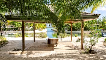 Un área de estar al aire libre con techo, una piscina, rodeada de palmeras y vistas despejadas al océano.