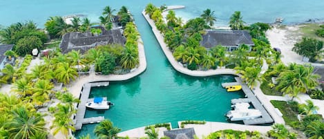 A resort with a central swimming pool, surrounded by palm trees and a beach.