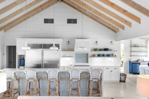 Una cocina moderna con armarios blancos, un refrigerador de acero inoxidable y un comedor con sillas de mimbre.