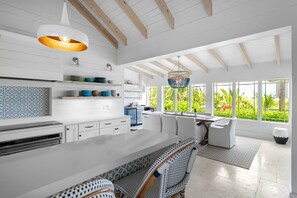 A modern kitchen with white cabinetry, a large island, and a dining area with bar stools. - Foxy Lady - Waterfront Luxury Villa sleeps 14 (Exuma)