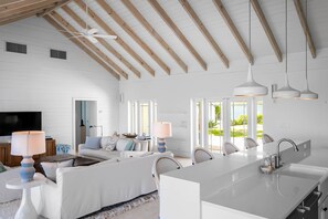 A spacious living room with a large white sofa, a dining area with a long island counter, and a ceiling fan. - Foxy Lady - Waterfront Luxury Villa sleeps 14 (Exuma)