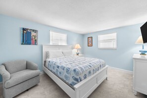 A bedroom with a bed, a chair, a nightstand, a lamp, and a dresser. - A10 - Gulf Breeze Getaway (Siesta Key)