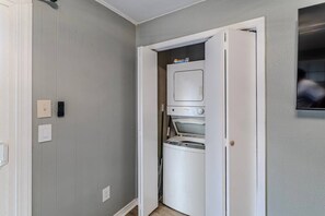 Ein Waschraum mit nebeneinander gestapelten Waschmaschine und Trockner, einer Tür zu einem anderen Raum und einem an der Wand montierten Lichtschalter.