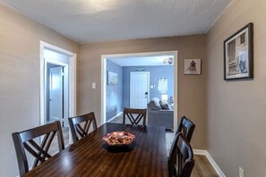 A dining room with a wooden table and chairs, a bowl of food, and a hallway leading to a living area with a couch and a door. - 1-story 3BR Near Medical Center & Downtown Houston (Houston)