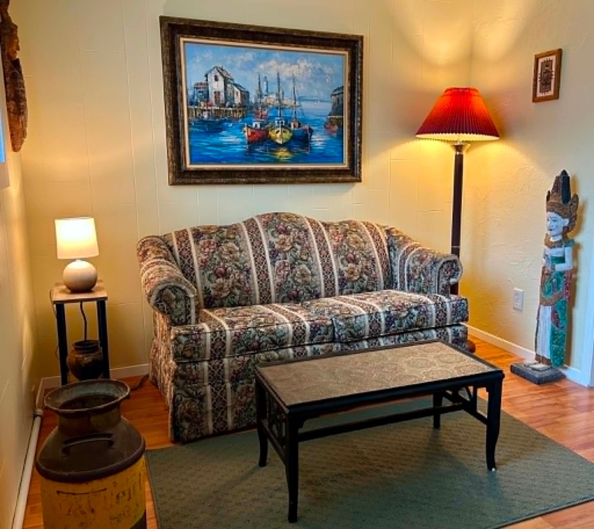 A living room with a patterned sofa, a coffee table, a lamp, a painting, and a statue.