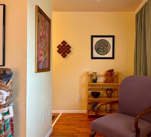 A living room with a wooden floor, a chair, a shelf with decorative items, and two framed pictures on the wall. - The Cozy Cottage: A Wanderer's Rest (Hot Springs)