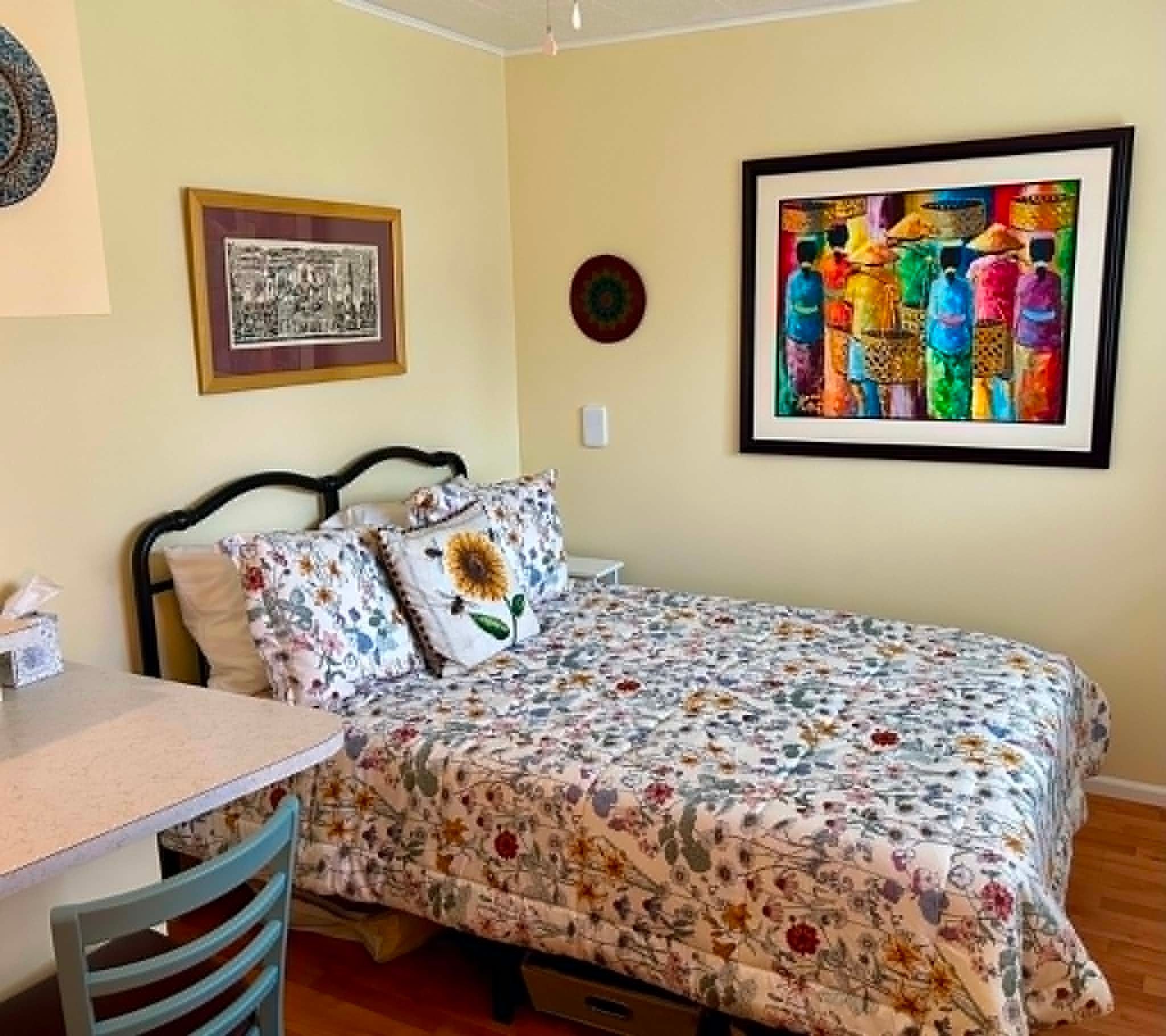 Une chambre à coucher comprenant un lit, une chaise, une table et deux œuvres d’art encadrées accrochées au mur.