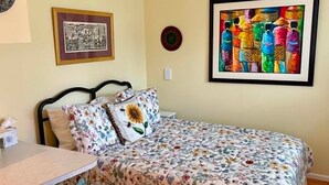 Une chambre à coucher comprenant un lit, une chaise, une table et deux œuvres d’art encadrées accrochées au mur.