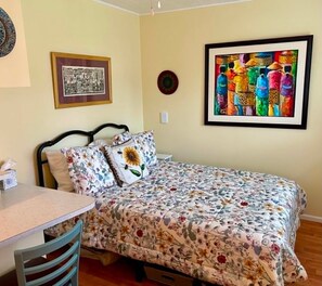 Ein Schlafzimmer mit einem Bett, einem Sessel, einem Tisch und zwei gerahmten Kunstwerken an der Wand.