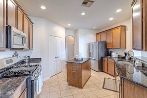 Una cucina moderna con piano cottura a gas, elettrodomestici in acciaio inossidabile, mobili in legno e pavimento piastrellato.