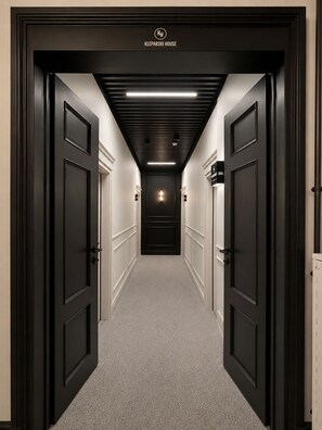 A hallway with black doors, a sign reading 'KLEPARSKI HOUSE,' and a light fixture on the ceiling. - Kleparski House (Kraków)